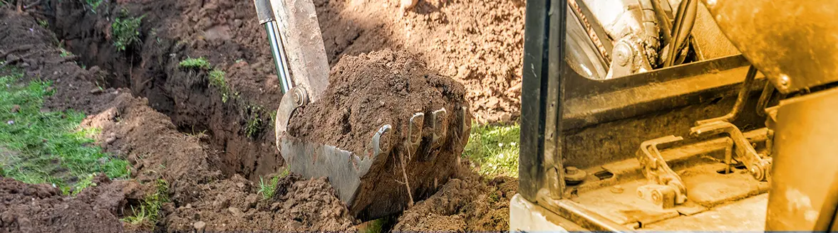 An excavator scoop is seen lifting a large amount of soil in a grassy area, with part of the machine's body visible on the right side, perhaps clearing the way for a pool removal.